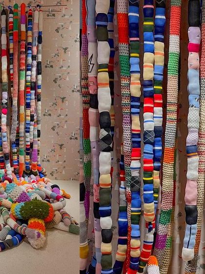 The 'Goblin Mode' sock installation, showing both the curtain of hanging socks and the pile of soft, tangled forms on the floor. The piece is an expression of whimsical, cocooned coziness.