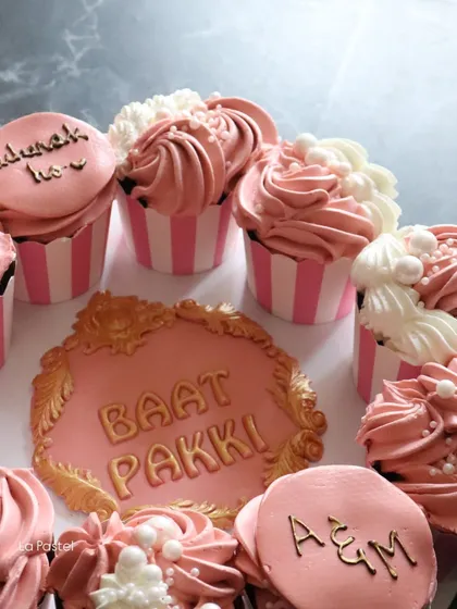 A side view of the 'Baat Pakki' cupcake platter, showing the fluffy pink and white frosting and custom toppers with the couple's initials.
