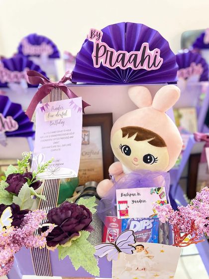 A closer look at a personalized birthday return favour for 'Praahi's' first birthday. Each box includes a thank you note, a plush toy, and some snacks.
