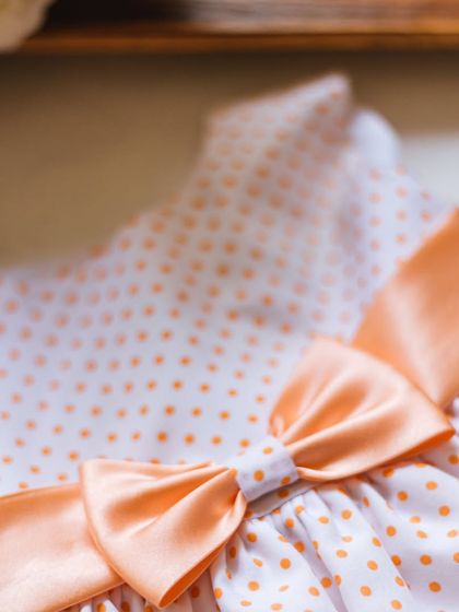 A close-up of this peach polka dot dress, showing the soft fabric and the perfectly constructed satin bow. It's a simple, timeless, and adorable design.