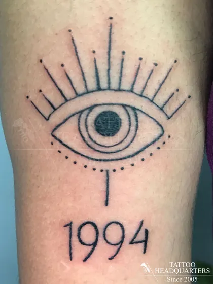 A stylized all-seeing eye tattoo with the year "1994" underneath, a personal and symbolic design.