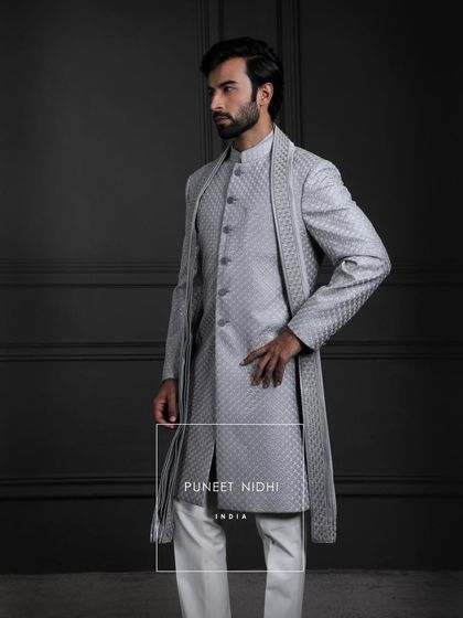 A fish-scale textured achkan with a matching stole sets a tone of regal artistry, layered over a silver sherwani with a lustrous sheen and sculpted with timeless structure.