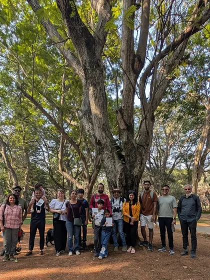 A group of friends and family, including a furry friend, posing for a photo under a magnificent tree. We are grateful for our wonderful community.