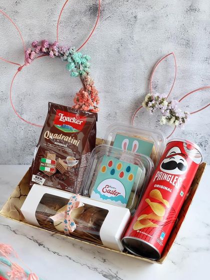 Our Easter gift hampers are packed with festive treats, including chocolates, Pringles, and a bar cake, all in a cute tray with bunny ears.
