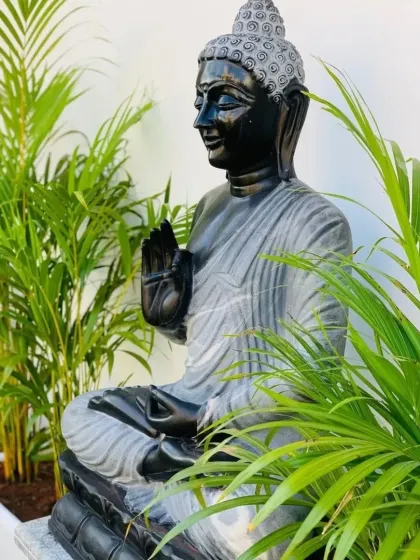 A close-up of a tropical-themed garden corner, featuring a Buddha statue framed by the bright green fronds of Areca palms. This styling choice is perfect for creating a resort-like feel at home.