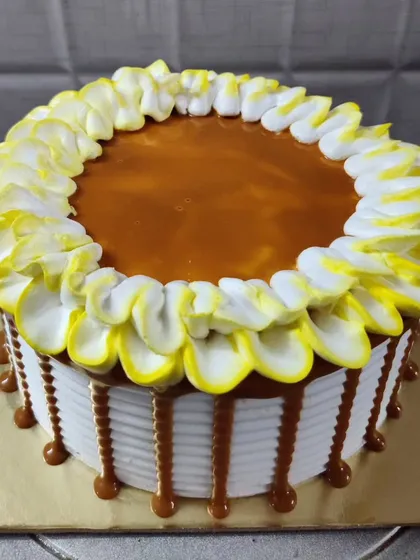 My butterscotch cake is a sweet and creamy treat. It features a smooth caramel topping, a border of yellow and white frosted petals, and a delicious caramel drip along the sides.