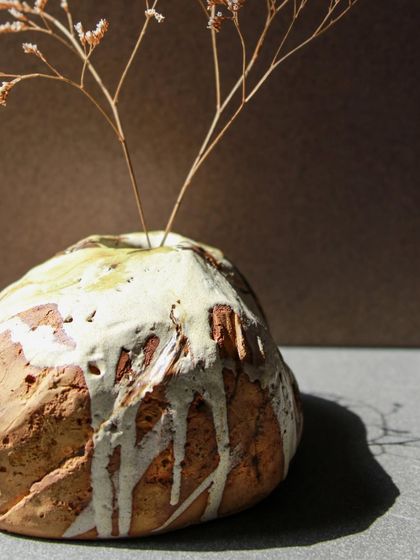 A round, rock like Kurinuki vase holding a delicate sprig, a beautiful contrast of textures and forms.