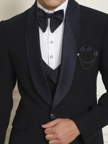 A close-up of the designer tuxedo, showing the detailed lapel, unique bow, and chain accessory. Get your "fit bhi style bhi" at our stores.