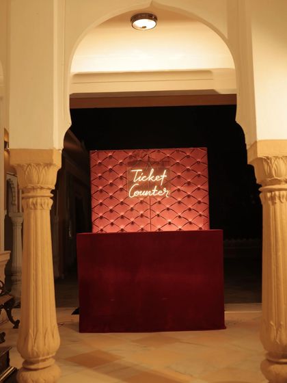 The "Ticket Counter" for the cinematic Sangeet, a fun and thematic element designed with a red velvet quilted backdrop and a neon sign.