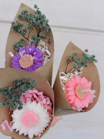 These mini candle bouquets are a perfect small token of affection. Each one features a single, detailed flower-shaped candle wrapped in rustic craft paper with dried flowers. They are a sweet and simple "just because" gift.