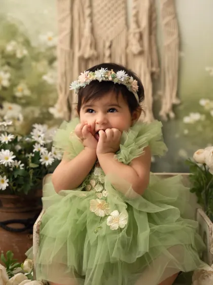 A baby girl in a beautiful green tulle dress looks up with a curious expression. This floral-themed sitter session has a magical, fairytale feel.