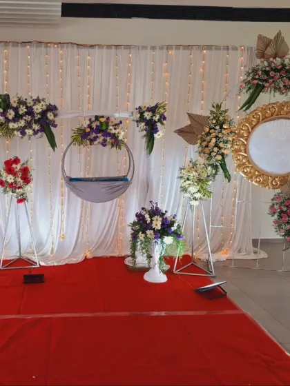 An elegant and modern naming ceremony setup with a hanging cradle, white drapes, and arrangements of white and purple flowers.