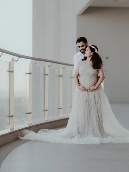 An elegant portrait of an expecting couple on a balcony. The mother-to-be is wearing a beautiful off-shoulder gown, creating a romantic and timeless maternity photograph.
