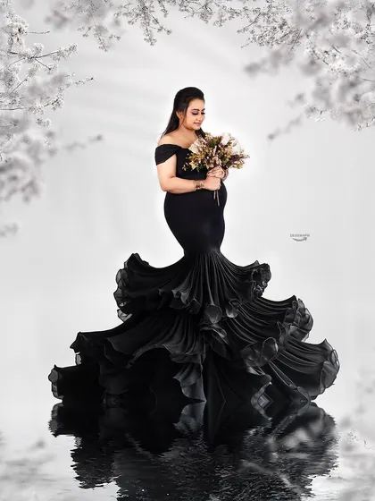 A stunning black and white composition featuring a dramatic ruffled mermaid gown. The floral frame and water reflection add layers of artistry to this elegant and timeless maternity portrait.