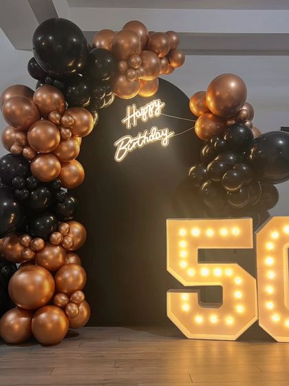 A clean and impactful setup for a 50th birthday. The simple black backdrop allows the neon sign, marquee numbers, and balloon garland to be the stars of the show.