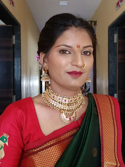 A classic look for a Maharashtrian bride in a green saree with a red border. The makeup features a bold red lip and defined eyes, paired with a traditional choker necklace.