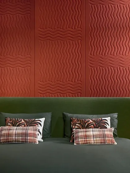This bedroom features a 3D wallcovering in a deep red, with quilted undulations creating a tactile surface. The pure wool material enhances both visual appeal and acoustic properties for a cozy, luxurious feel.