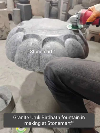An artisan is seen polishing a granite urli birdbath fountain in our workshop. This best-selling design is hand-carved into a floral shape from a single block of granite.