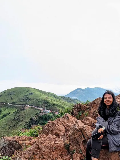 A traveler sitting on the rocky edge of Mullayanagiri peak, enjoying the vast, green landscape of Chikmagalur.