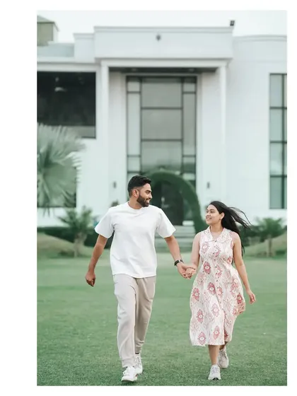 A joyful shot of the couple running hand-in-hand on a beautiful lawn in front of a modern house.