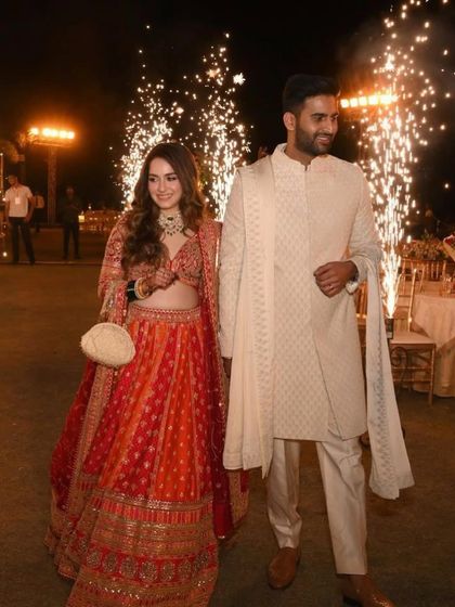 A fairytale entrance. This bride's red and orange lehenga is paired with a soft, romantic makeup look that glows beautifully under the celebratory sparklers, making for a truly magical wedding moment.