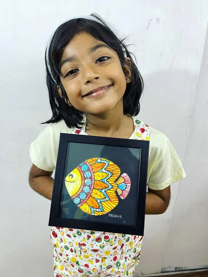One of our youngest artists, just five years old, proudly displaying her colorful Madhubani fish painting. Our classes are designed to be fun and accessible for children, helping them build confidence and skill.