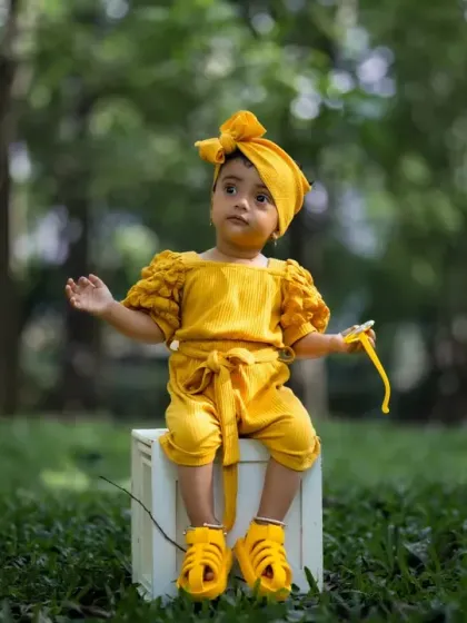 A stylish toddler in a bright yellow outfit, posing confidently during her outdoor session. The natural greenery makes the colors pop.