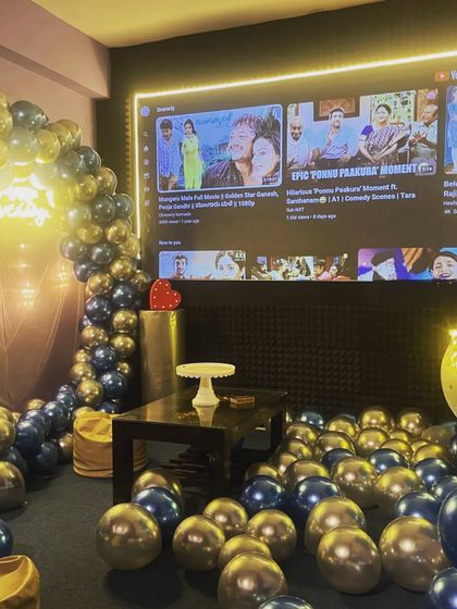 The theatre is all set for a birthday party, with a balloon arch, neon sign, and the YouTube homepage on screen, ready for the guest of honor to pick their favorite videos.