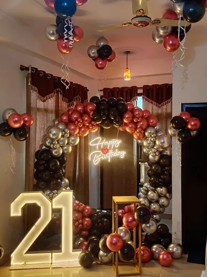 A bold and stylish 21st birthday party decoration. This setup features a circular balloon arch in black, red, and silver, with a neon sign and large light-up numbers.