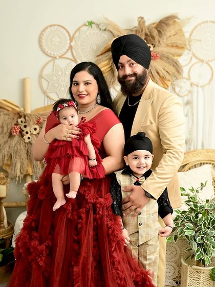 A stunning family of four, dressed elegantly for their newborn's first photoshoot. The rich red and gold tones create a regal and celebratory feel.