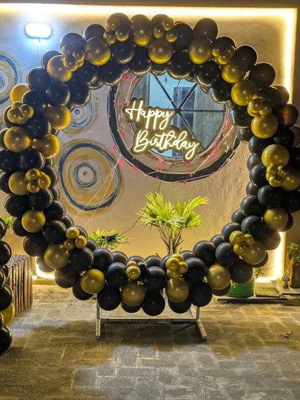 A full circular balloon arch in black and gold set up on a patio, with a neon sign creating a stunning centerpiece.
