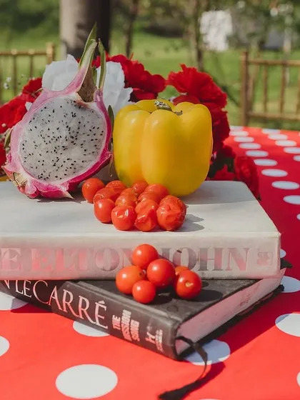 A creative centerpiece for the 'La Tomatina' Haldi, featuring cherry tomatoes, dragon fruit, and a yellow bell pepper arranged on a stack of books. The polka dot tablecloth adds a playful touch.