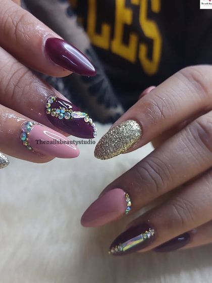 A stunning bridal nail inspiration set, featuring a mix of deep wine and soft pink polish, gold glitter, and intricate rhinestone designs.