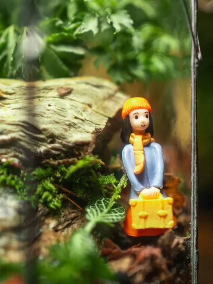 A close-up of the traveler figurine with her yellow suitcase, standing amidst the mossy terrain. These little details are what make my terrariums so special and personal.