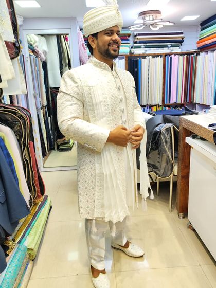 A smiling groom in his all-white embroidered sherwani, complete with a matching safa. The side view shows the elegant drape of the stole.