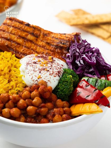 A detailed look at our Chicken Shish Tawook Bowl, showcasing the grilled chicken, seasoned chickpeas, turmeric rice, and a dollop of creamy garlic yogurt.