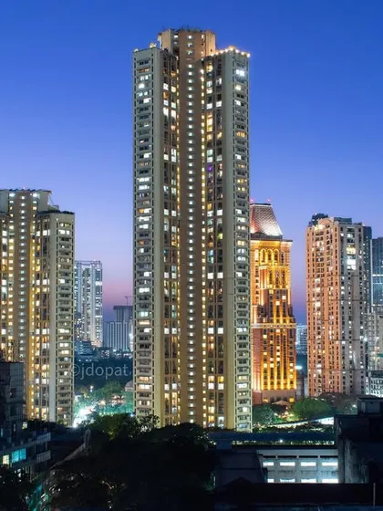 Tall residential towers in Mumbai are lit up against a deep blue twilight sky, showcasing the city's vertical growth and modern architecture.