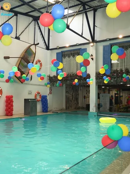 The pool area decorated with clusters of colorful balloons hanging from the ceiling, ready for a fun-filled birthday party.