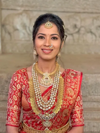 A radiant red saree look, featuring a classic nose pin and traditional hair ornaments. The makeup is soft yet striking with a skin-like finish.