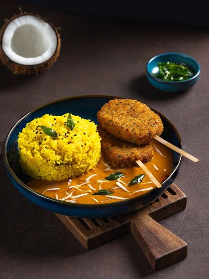 A South Indian inspired meal bowl with coconut curry, lemon rice, and vegetable cutlets on skewers.