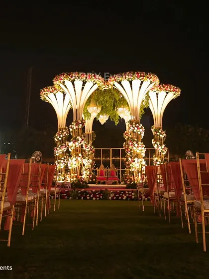 An overview of a grand outdoor wedding mandap at night. The illuminated structures, floral arrangements, and perfectly aligned guest seating demonstrate our ability to transform large lawns into spectacular wedding venues.