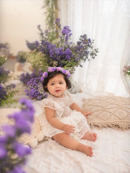 The birthday girl sits among pillows and purple flowers, looking so sweet and thoughtful in her beautiful studio setup.