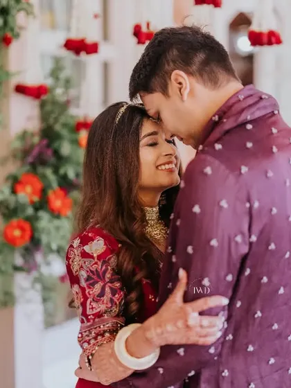 Summer love in full bloom. A tender moment between the couple during their Mamera ceremony, surrounded by vibrant red and orange floral decor that perfectly complements the warmth of their connection.
