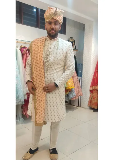This groom is wearing a stylish ivory sherwani with subtle gold patterns. The look is completed with a peach-colored stole and a matching pagri.