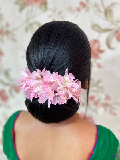 A classic, sleek donut bun adorned with a simple row of pink flowers, a very clean and elegant look.