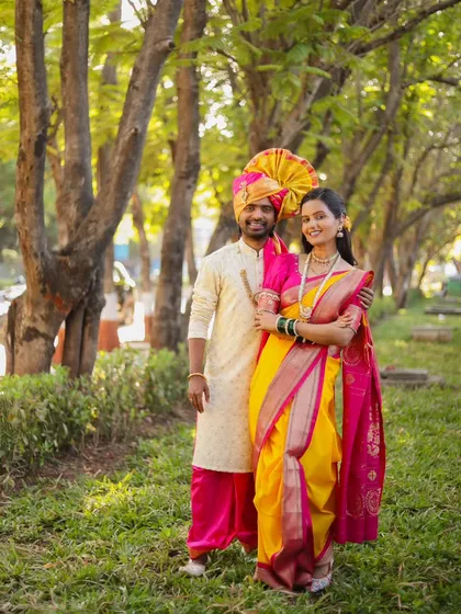 A full-length portrait of a couple in traditional Maharashtrian attire, standing together in a lush, green park.