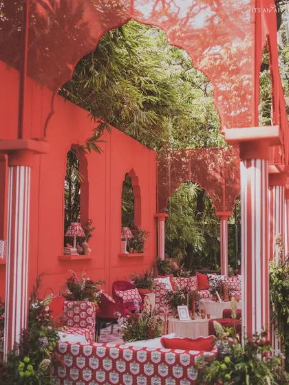 A view through the red arches, showcasing the layered design with custom-printed textiles and striped pillars.