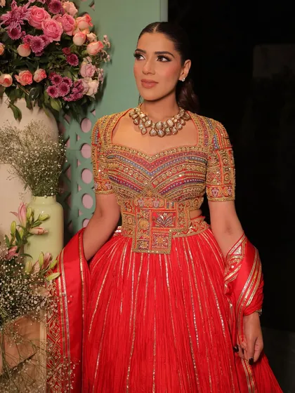 Another angle of this stunning red anarkali look, set against a beautiful floral backdrop. The makeup enhances her features with a subtle smokey eye.