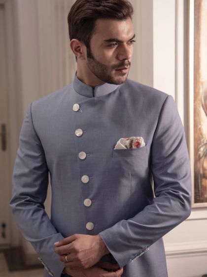 A sherwani in a cool, powder blue. The contrasting white buttons and patterned pocket square add a touch of modern flair to this classic, elegant silhouette.