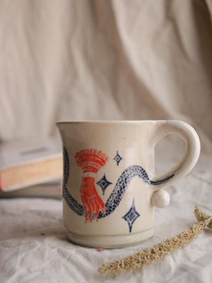 This sgraffito mug features a mystical hand and a serpent, a design that feels both ancient and magical. The contrast between the carved black snake and the vibrant red hand makes it a powerful piece.